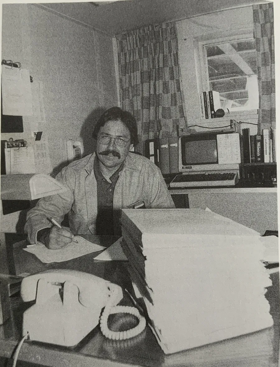 Captain Mike at his desk aboard the tanker Exxon Benicia, with a stack of paperwork, a desk phone and an early computer terminal