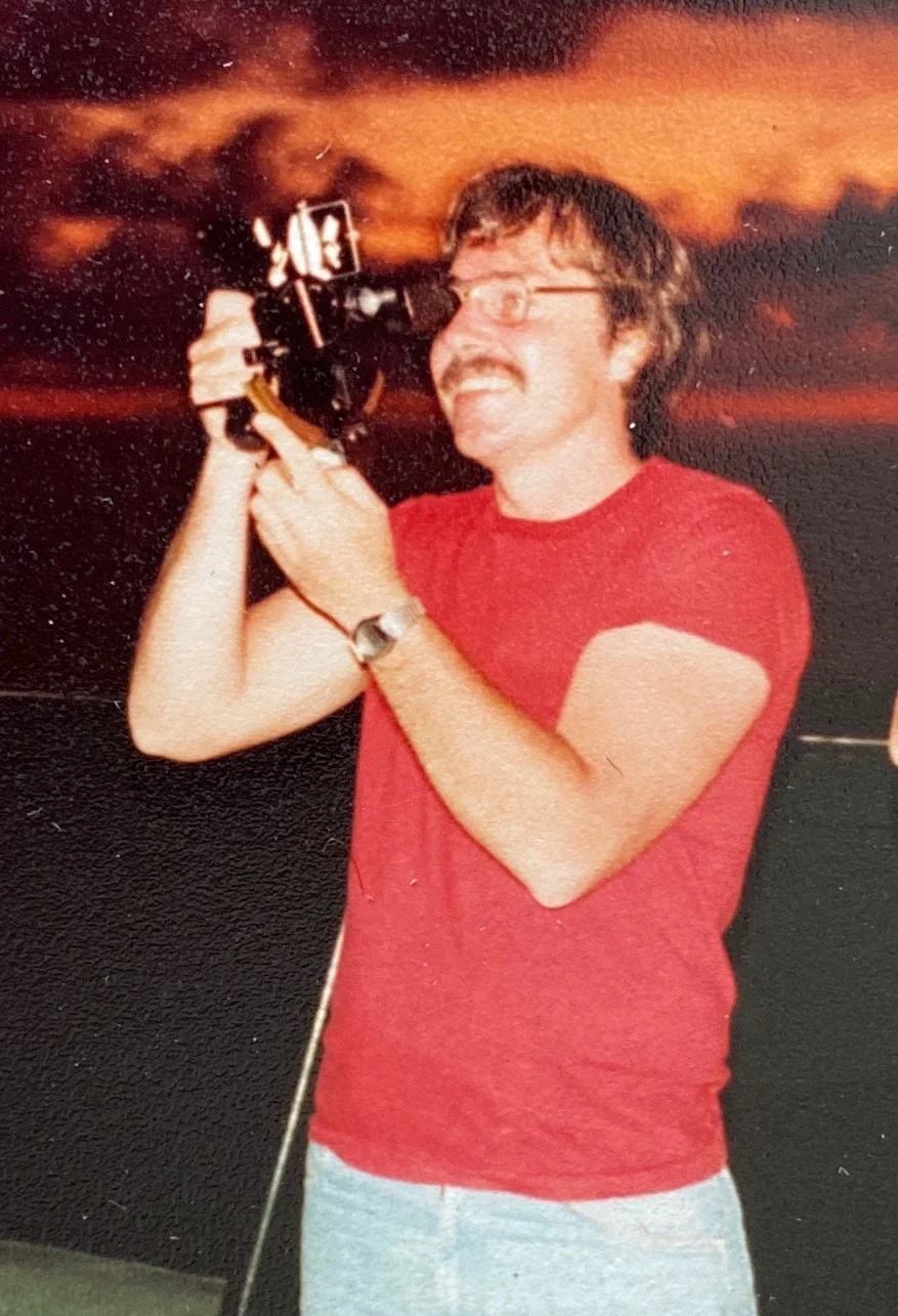 Young Mike in a red T-shirt taking a sextant sight on deck at twilight